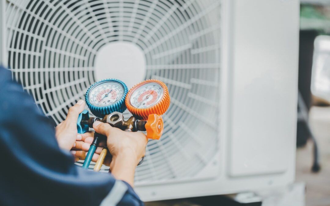 A technician using a manifold gauge set to check refrigerant levels on an outdoor AC unit.