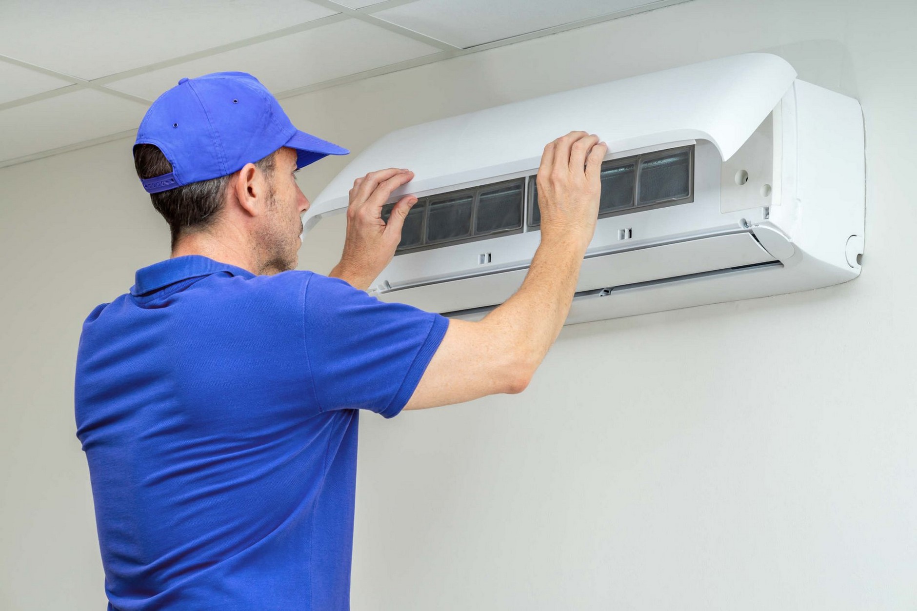 A technician performing maintenance on a wall-mounted air conditioning unit.